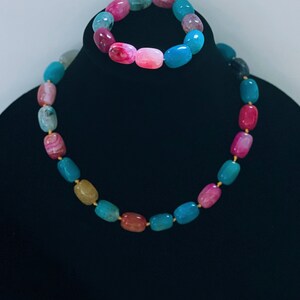 Pu&ograve; includere: Un set di collana e braccialetto in agata multicolore. La collana e il braccialetto sono realizzati con perline ovali in tonalit&agrave; di rosa, blu, verde e giallo.