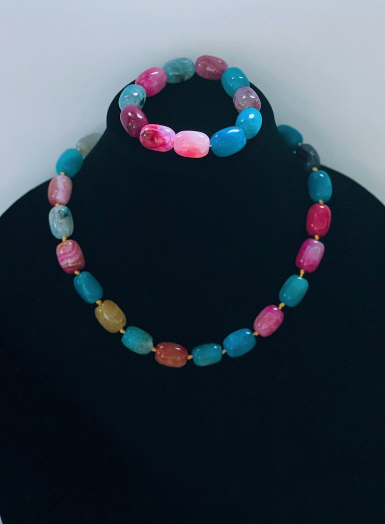 Pu&ograve; includere: Un set di collana e braccialetto in agata multicolore. La collana e il braccialetto sono realizzati con perline ovali in tonalit&agrave; di rosa, blu, verde e giallo.