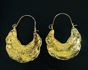 May include: A pair of gold hoop earrings with a textured, hammered finish. The earrings are large and have a crescent shape.