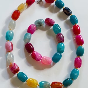 Pu&ograve; includere: Un set di collana e braccialetto in pietra di agata colorata. La collana &egrave; realizzata con perline ovali in tonalit&agrave; di rosa, rosso, blu, giallo e bianco. Il braccialetto &egrave; realizzato con perline ovali pi&ugrave; piccole in colori simili.