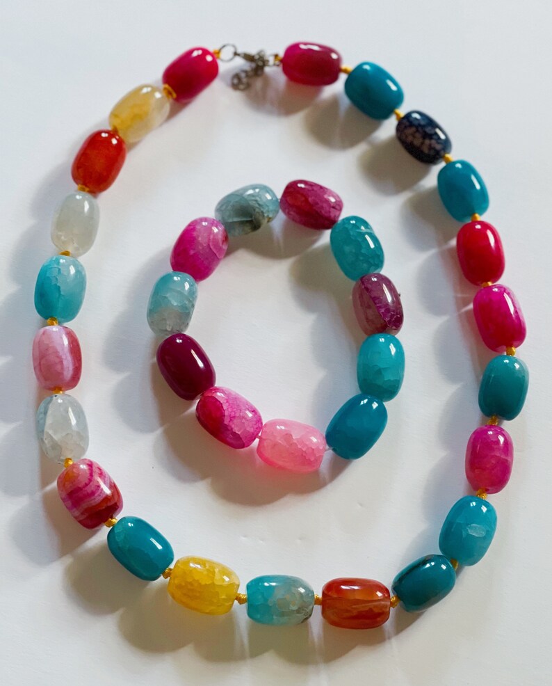 Pu&ograve; includere: Un set di collana e braccialetto in pietra di agata colorata. La collana &egrave; realizzata con perline ovali in tonalit&agrave; di rosa, rosso, blu, giallo e bianco. Il braccialetto &egrave; realizzato con perline ovali pi&ugrave; piccole in colori simili.
