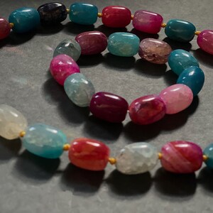 Pu&ograve; includere: Un set di collana e braccialetto con perline di agata multicolori. La collana e il braccialetto sono realizzati con perline ovali in tonalit&agrave; di rosa, rosso, blu e bianco.