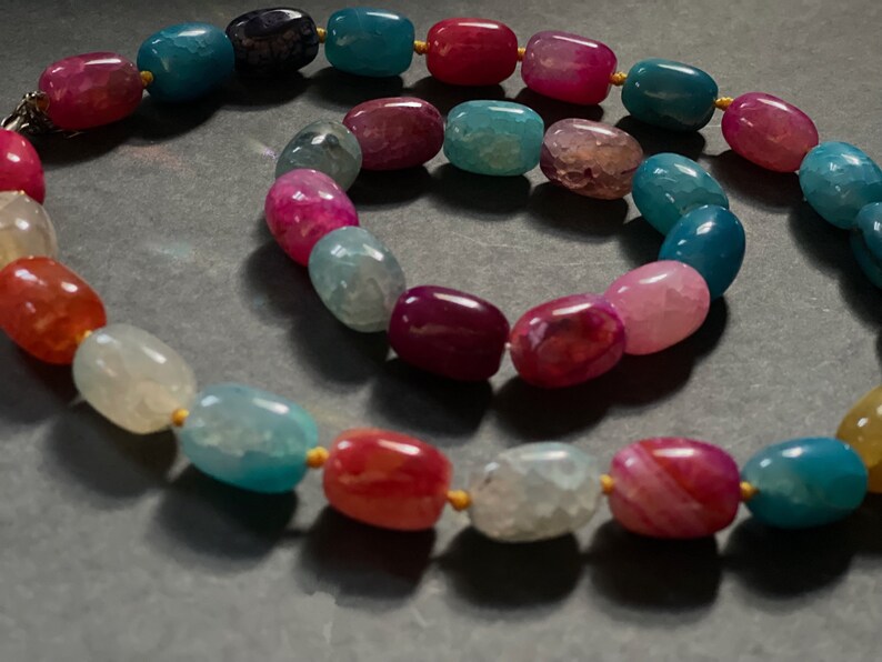 Pu&ograve; includere: Un set di collana e braccialetto con perline di agata multicolori. La collana e il braccialetto sono realizzati con perline ovali in tonalit&agrave; di rosa, rosso, blu e bianco.