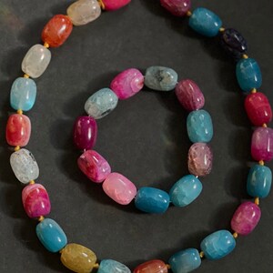 Pu&ograve; includere: Un set di collana e braccialetto con perline di agata colorate. La collana e il braccialetto sono realizzati con perline di agata multicolori con un filo dorato che le attraversa.