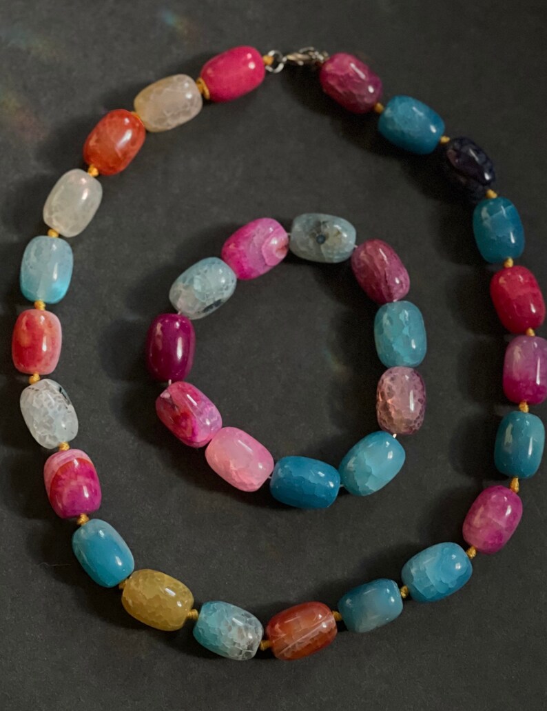 Pu&ograve; includere: Un set di collana e braccialetto con perline di agata colorate. La collana e il braccialetto sono realizzati con perline di agata multicolori con un filo dorato che le attraversa.