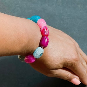 Pu&ograve; includere: Un braccialetto di perline di agata colorate con perline rosa, blu e bianche. Il braccialetto &egrave; realizzato con pietre naturali e ha un aspetto unico e organico.