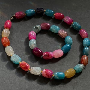 Pu&ograve; includere: Un set di due collane in pietra di agata con una miscela di colori rosa, blu e verde. Le collane sono fatte di perline ovali con accenti dorati.