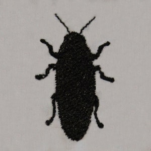 Peut inclure: Silhouette brodée noire d'un scarabée sur un fond de tissu blanc.