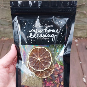 Może przedstawiać: Czarny, zamykany worek z białą etykietą z napisem "Kitchen Conjure new home blessing Simmer Pot Potpourri". Worek zawiera suszone cytrusy, płatki r&oacute;ż i zioła.