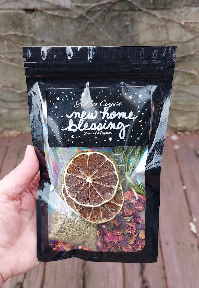 Może przedstawiać: Czarny, zamykany worek z białą etykietą z napisem "Kitchen Conjure new home blessing Simmer Pot Potpourri". Worek zawiera suszone cytrusy, płatki r&oacute;ż i zioła.