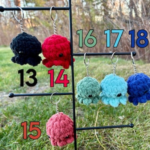 May include: A display of 10 crocheted octopus keychains in various colors, including black, red, green, blue, and teal. The keychains are numbered 13 through 18.