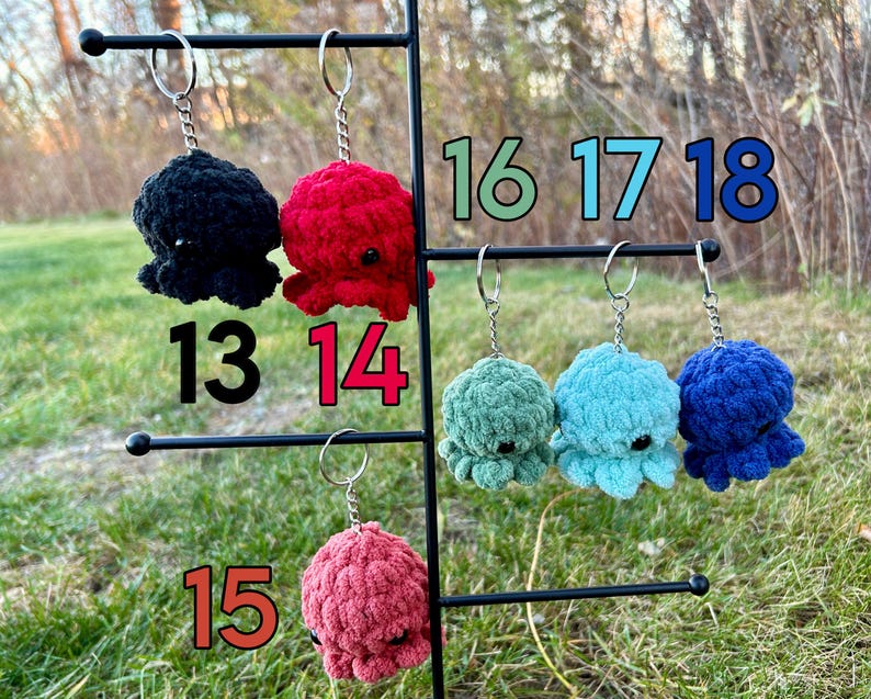 May include: A display of 10 crocheted octopus keychains in various colors, including black, red, green, blue, and teal. The keychains are numbered 13 through 18.