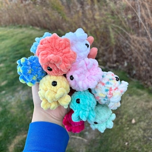 Puede incluir: Una colección de juguetes de peluche de crochet de varios colores, formas y tamaños. Los juguetes están hechos de hilo suave y esponjoso y tienen ojos negros.