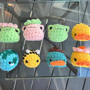 May include: Eight crocheted stuffed animals in various colors and shapes, including a frog, a bee, a turtle, a duck, and a platypus. The animals are all small and have a cute, cartoonish appearance.