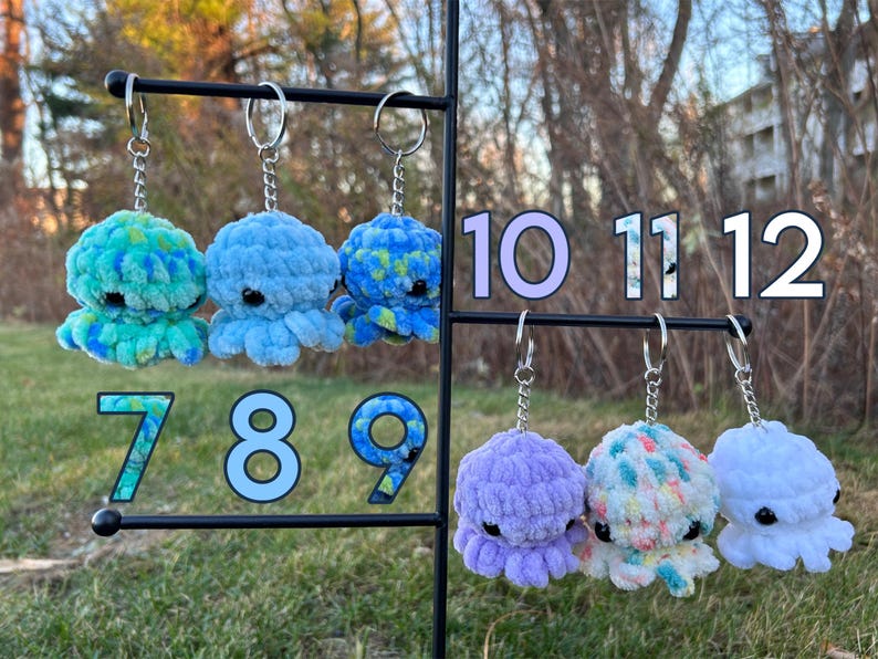 May include: Twelve crocheted octopus keychains in various colors, including blue, green, purple, and white. The keychains are displayed on a metal rack with numbers 7 through 12.