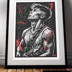 May include: A framed black and white print of a guitarist with red highlights. The artwork features the word "Fender" on the guitar strap. The image is set against a black background with a white border. The frame is black.