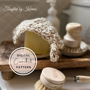 Könnte beinhalten: Ein gehäkelter Seifenspender in Naturtönen bedeckt ein Seifenstück. Das Bild enthält eine Holzschale, eine Spülbürste und den Text "Digital Crochet Pattern". Auf der Seife steht das Wort "Juice".