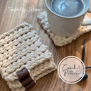 May include: A stack of off-white crochet coasters featuring a thick, textured yarn weave and a dark brown leather tag. One coaster sits under a white ceramic mug filled with a dark liquid. The text Tangled by Karina and Crochet Pattern appear.