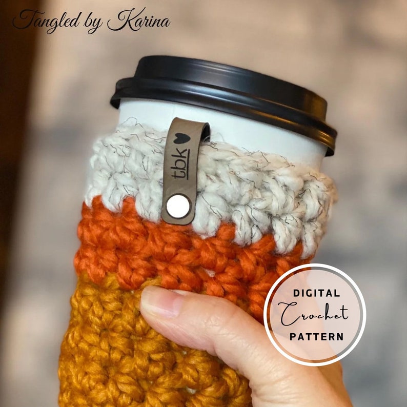 May include: A crocheted coffee cup cozy in orange, brown, and white with a leather strap that says "tbk" with a heart. The cozy is being held by a hand. The text "DIGITAL CROCHET PATTERN" is in a circle on the right side of the image.