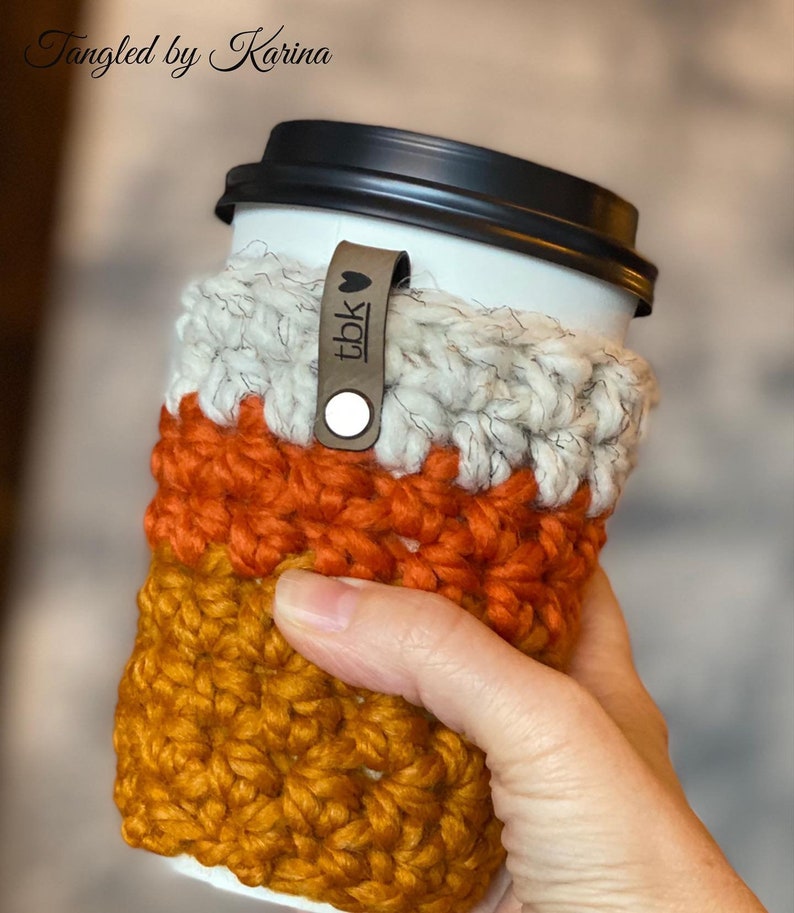 May include: A crocheted coffee cup cozy in orange, white, and brown with a leather strap that says "tbk" with a heart.