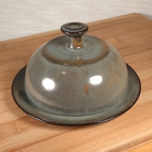 May include: A white ceramic mug with a black handle and the text "But First, Coffee" in a handwritten style. The mug is on a white surface. The mug is approximately 4 inches tall.