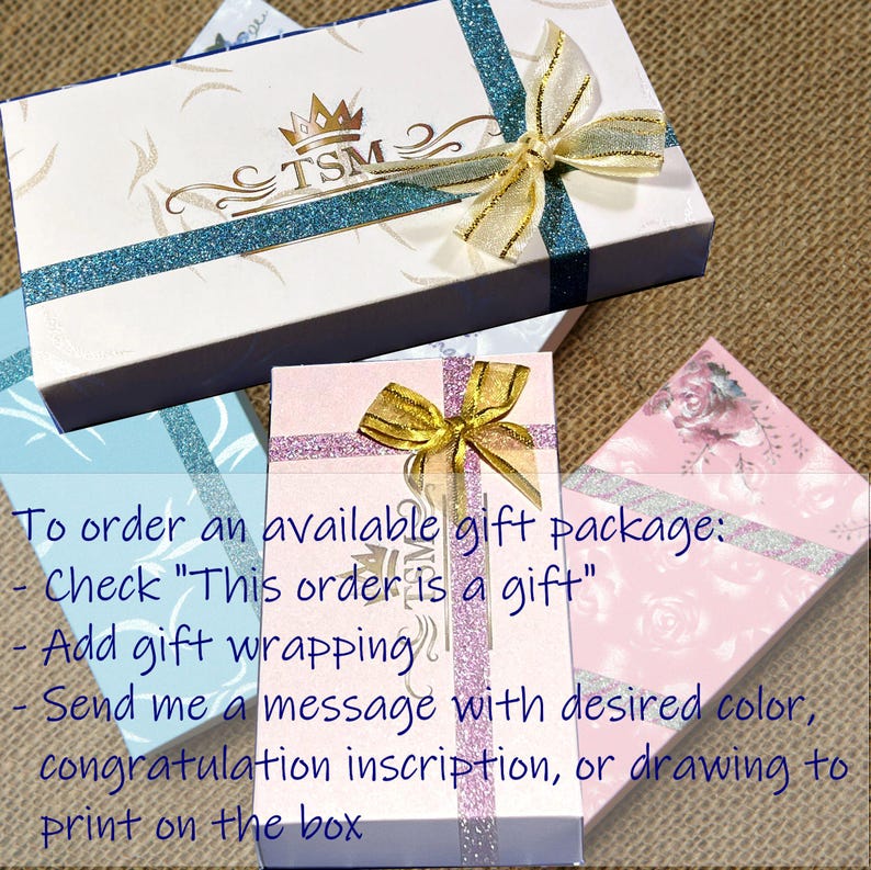 K&ouml;nnte beinhalten: Rechteckige Geschenkboxen in Wei&szlig;, Hellblau und Rosa, jeweils mit glitzerndem Band, goldener Schleife und TSM-Logo. Auf dem Bild sind Anweisungen zum Bestellen eines Geschenkpakets sowie Optionen f&uuml;r die Geschenkverpackung aufgedruckt.