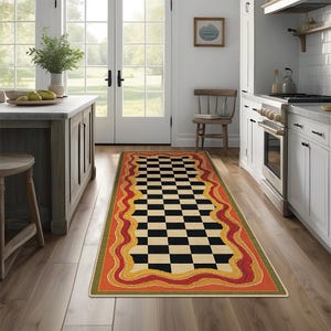 May include: A rectangular kitchen rug featuring a black and cream checkerboard design. The rug has a wavy border with orange, yellow, and red accents, and a green outer edge. The rug is placed on a wooden floor in a kitchen setting.