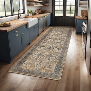 May include: A long, rectangular rug with an ornate, floral pattern in beige, grey, and gold tones. The rug has a dark grey border and is placed on a wooden floor in a kitchen setting.