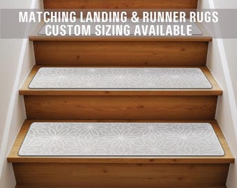 May include: A set of gray stair treads with a white floral pattern. The treads are shown on a wooden staircase. The text "Matching Landing & Runner Rugs Custom Sizing Available" is displayed above the staircase.