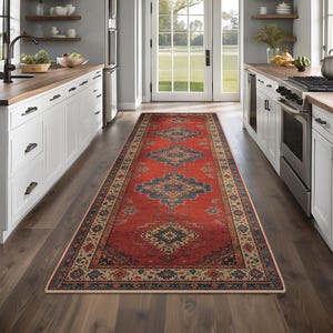 Puede incluir: Una alfombra pasillera rectangular larga con una base de color rojo vibrante y patrones geométricos intrincados en azul marino, crema y oro mate. La alfombra tiene un borde decorativo ancho con motivos florales sobre un suelo de madera oscura.