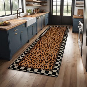 May include: A long, rectangular rug with a leopard print design in shades of orange and black. The rug has a black and white checkered border, adding a contrasting element. The rug is placed in a kitchen setting.