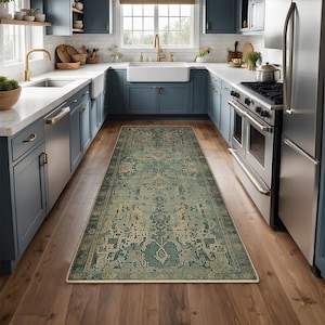 Puede incluir: Una alfombra rectangular de aspecto envejecido en una cocina. La alfombra presenta un diseño floral en tonos turquesa y beige con un borde crema. La cocina tiene gabinetes azules, electrodomésticos de acero inoxidable y pisos de madera.