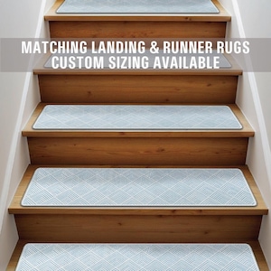 Puede incluir: Un conjunto de peldaños de escalera con estampado azul y blanco con borde blanco. Los peldaños están en una escalera de madera. El texto "Matching Landing & Runner Rugs Custom Sizing Available" está en la parte superior de la imagen.