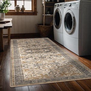 May include: A rectangular area rug featuring a distressed pattern in shades of cream, charcoal grey, and muted gold. The rug has a wide, dark grey border with intricate floral motifs and a central field filled with ornate, symmetrical scrollwork designs.