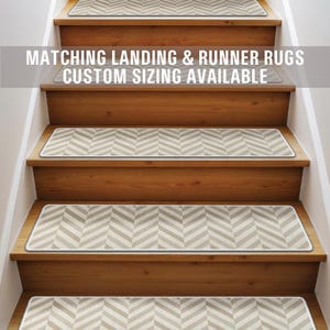 Puede incluir: Un conjunto de peldaños de escalera con estampado de chevron beige y blanco con un borde blanco. El texto "Matching Landing & Runner Rugs Custom Sizing Available" se muestra sobre las escaleras.