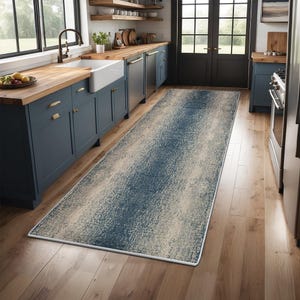 Puede incluir: Una alfombra de pasillo rectangular larga con un patrón texturizado y desgastado en tonos azul marino profundo y crema. La alfombra tiene un borde blanco acabado y está colocada sobre un suelo de madera clara en una cocina con armarios azules.