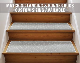 May include: A set of gray chevron patterned stair treads with white borders. The treads are on a wooden staircase. The text "Matching Landing & Runner Rugs Custom Sizing Available" is at the top of the image.