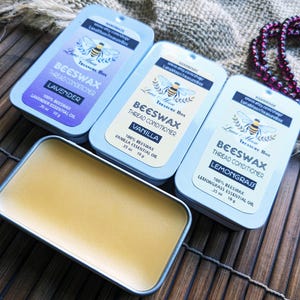 May include: Three small metal tins containing beeswax thread conditioner in lavender, vanilla, and lemongrass scents. Each tin has a label with the Luna Moon Treasure Box logo and the scent name. The tins are sitting on a woven bamboo mat.