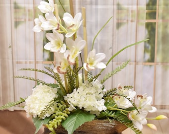 May include: A white orchid and hydrangea floral arrangement in a gold bowl. The arrangement features white flowers with green leaves and stems.
