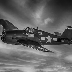 May include: A black and white photograph of a vintage military aircraft in flight. The plane is a Grumman F6F Hellcat, a fighter plane used by the United States Navy during World War II. The plane is flying through a cloudy sky, and the sun is shining through the clouds. The plane has a large star on the side, and the words "Missy II" are painted on the fuselage.