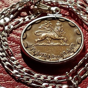 May include: A silver chain necklace with a pendant featuring a bronze coin with a lion and a flag. The coin has the text "Ethiopia" in Amharic.