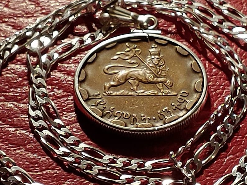 May include: A silver chain necklace with a pendant featuring a bronze coin with a lion and a flag. The coin has the text "Ethiopia" in Amharic.