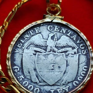 May include: A gold chain necklace with a silver coin pendant featuring an eagle and shield design. The coin has the text "CINCO CENTAVOS" and "G. 5.000. LEY" around the edge.