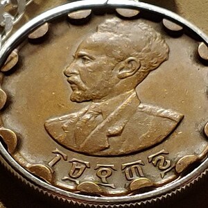 May include: A bronze coin with a portrait of a man with a beard and a crown. The coin has the text "I  ETHIOPIA" around the edge.