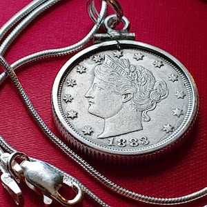 May include: A silver chain necklace with a silver pendant featuring a 1883 Liberty Head nickel coin. The coin has a profile of a woman's head with the word "LIBERTY" above it.