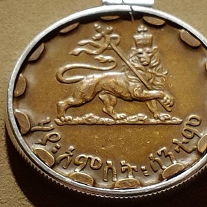 May include: A gold-colored coin with a lion holding a staff and a crown on its head. The coin has Ethiopian writing around the edge.