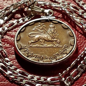 May include: A silver chain necklace with a round pendant featuring a bronze-colored lion with a crown and a spear. The pendant has the text "Ethiopia" in Amharic script.