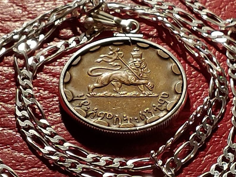 May include: A silver chain necklace with a round pendant featuring a bronze-colored lion with a crown and a spear. The pendant has the text "Ethiopia" in Amharic script.