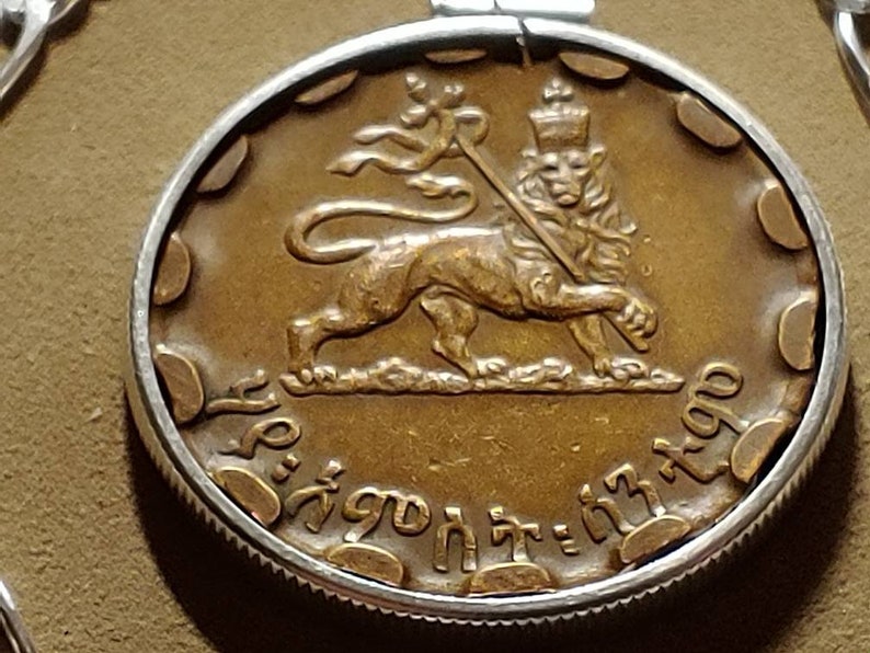 May include: A gold-colored coin with a lion holding a staff and a crown on its head. The coin has Ethiopian writing around the edge.
