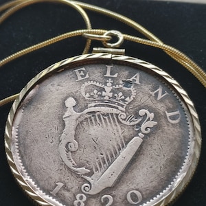 May include: A silver coin pendant with a gold chain. The coin features a harp and the text "ELAND 1820".